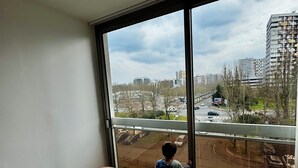 Une pièce dotée d’une grande fenêtre donnant sur un parking et des immeubles.