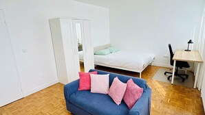 Une chambre à coucher avec un lit, un canapé bleu orné de coussins roses, un bureau avec une chaise et une armoire.