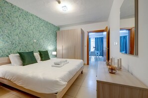 Relax in a spacious room with a large bed, wooden wardrobe, and a mirror above, offering a comfortable retreat with a balcony and a small table.