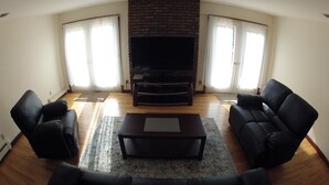 A living room with a fireplace, two black sofas, a coffee table, and a flat-screen TV.