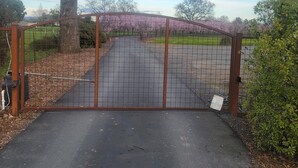A gated driveway leading to a property with a large tree and a view of a park with blooming trees. - Charming country cottage in lovely Santa Rosa on 8 acres (Santa Rosa)