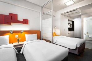 Two single beds with white bedding and a wooden headboard, plus a seating area with a chair and table.