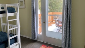 Ein Zimmer mit einem weißen Etagenbett, einer Schiebetür zu einem Außenbereich mit Holzterrasse und einem Stuhl.