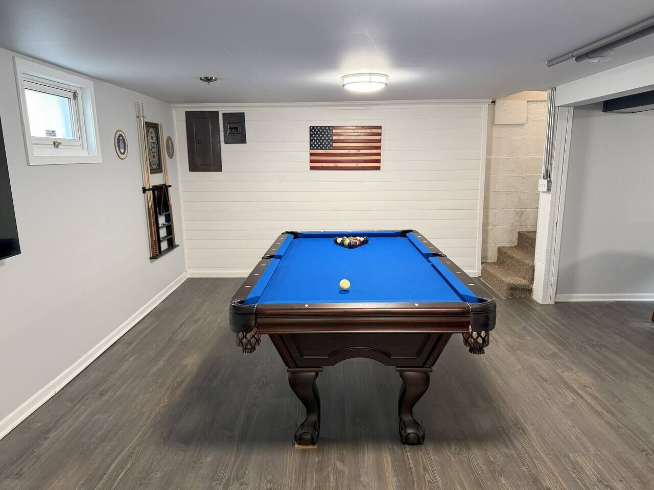 A pool table in a room with a wooden floor, white walls, and an American flag.