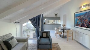 A modern living room with a sofa, a blue armchair, a dining area with a table and chairs, and a kitchen in the background. - Pliny Suite 33 -N.7- (Milano)