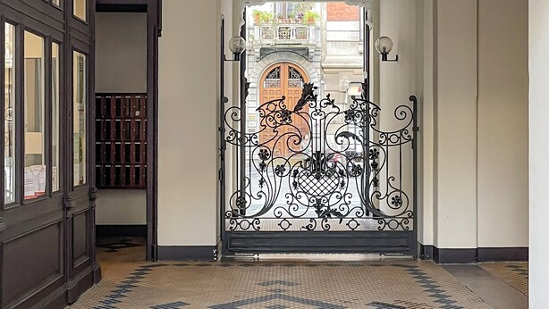A hallway with ornate ceiling and patterned floor tiles, leading to a door with a wrought iron gate. - Pliny Suite 33 -N.7- (Milano)