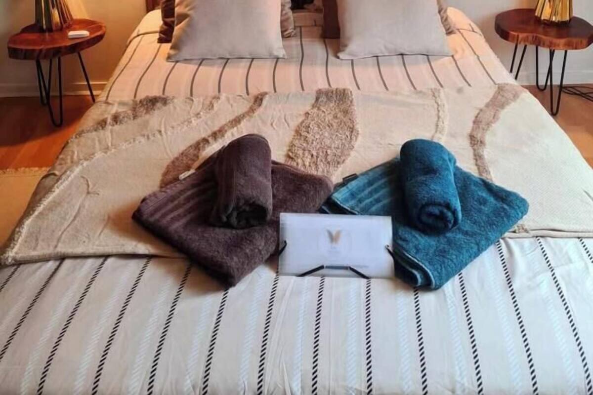 Een net opgemaakt bed met gestreepte lakens, twee kussens en een opgevouwen handdoek.