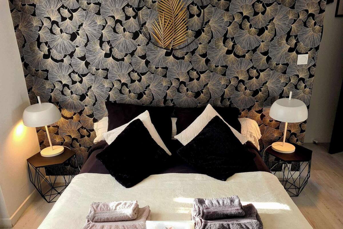 Een net opgemaakt bed met twee kussens, twee bedlampen en opgevouwen handdoeken op een witte laken.