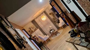 Ein modernes Wohnzimmer mit Backsteinwand, einem Essbereich mit Tisch und Stühlen sowie einer Küchenzeile mit Kühlschrank und Schränken.