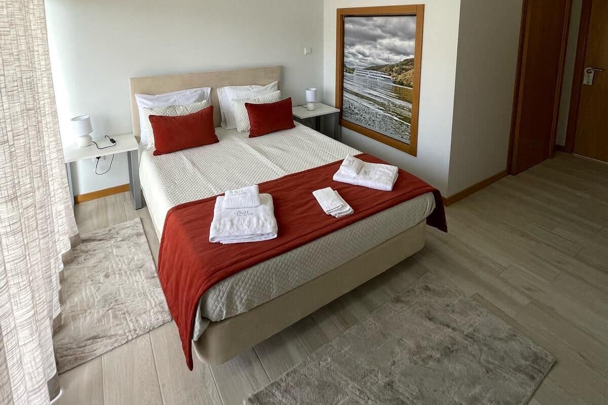Un dormitorio moderno con una cama grande, una mesita de noche, un tocador, un cuadro en la pared y una puerta de madera.