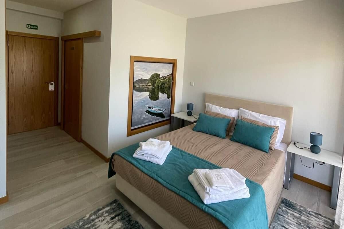 Un dormitorio con cama, mesita de noche, un cuadro y una puerta.