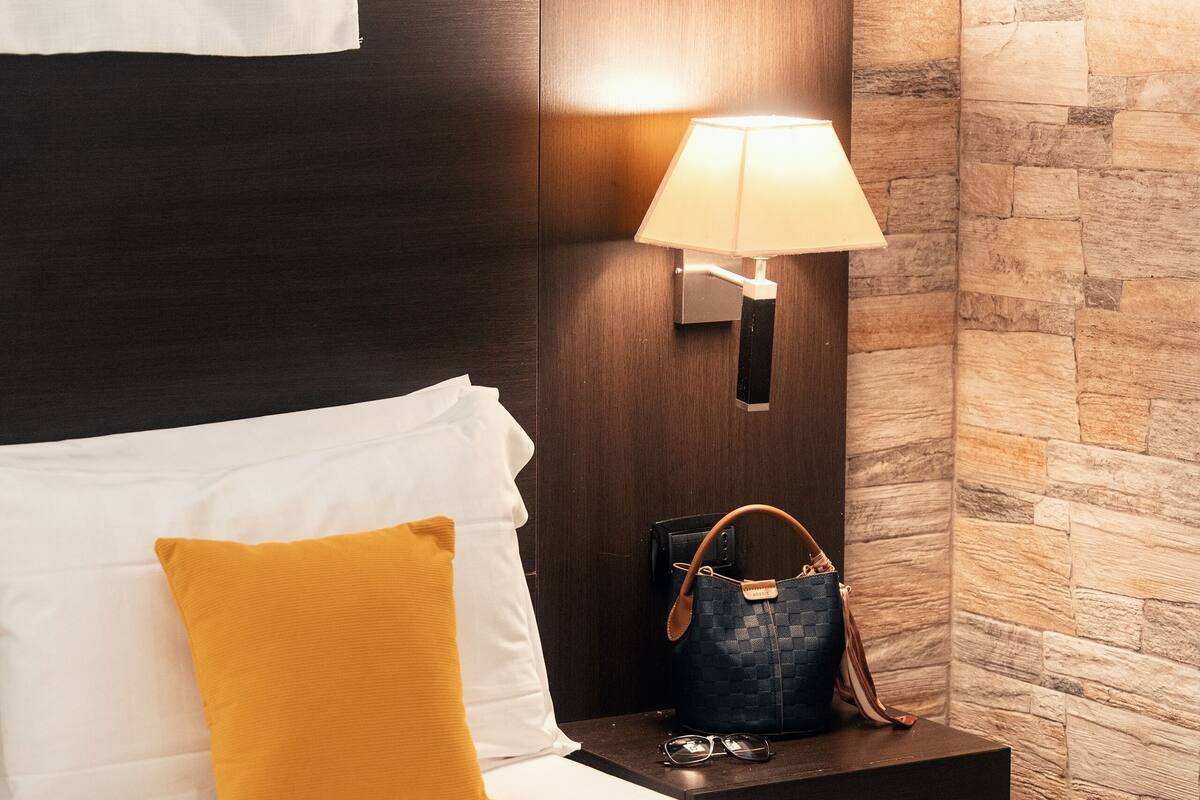 A hotel room with a bed, a nightstand, a lamp, and a stone wall.