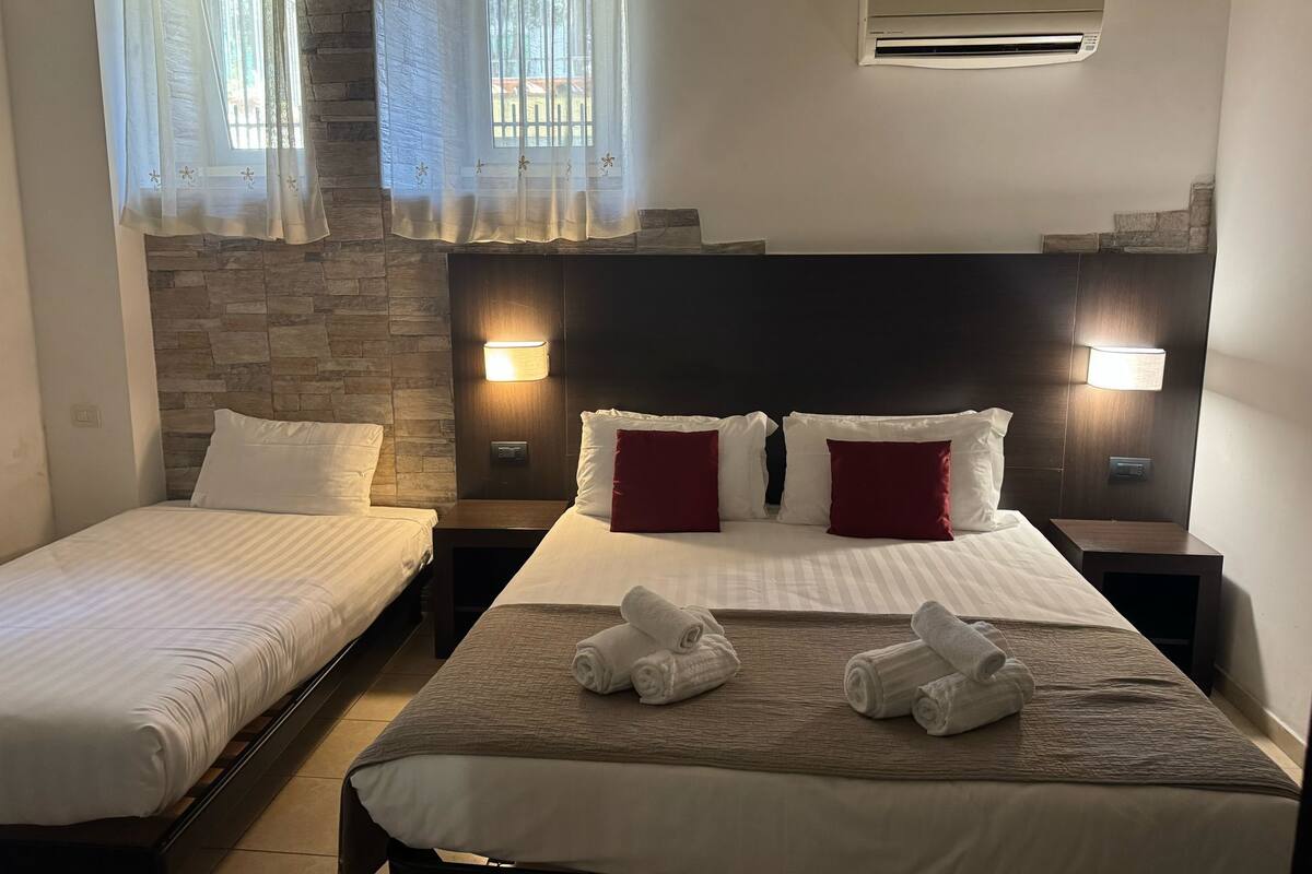 A hotel room with two beds, a stone wall, and a window with sheer curtains.