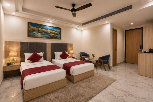 A hotel room with two beds, a desk, a chair, a painting, and a ceiling fan. - Hotel West End Mahipalpur Delhi IGI (New Delhi)