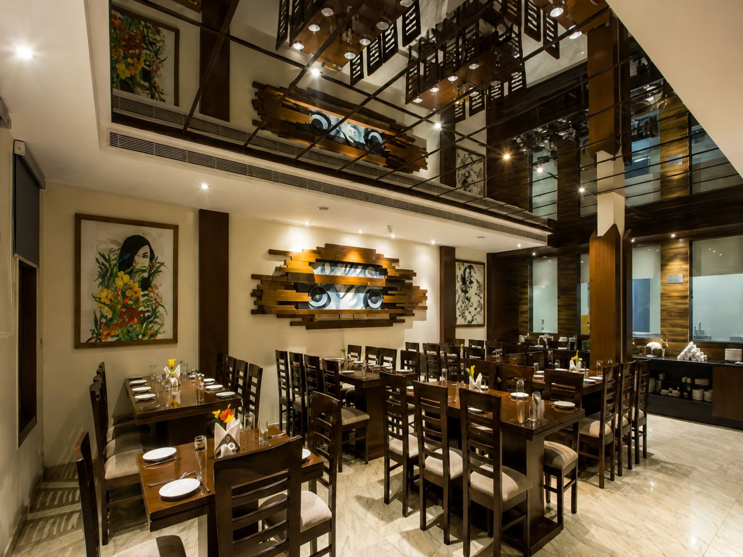 A dining area with multiple tables and chairs, a decorative wall with abstract art, and a staircase with wooden railings.