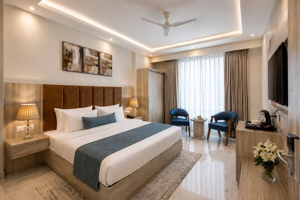 A modern hotel room with a large bed, bedside tables, a desk, chairs, a TV, and artwork on the wall. - Hotel West End Mahipalpur Delhi IGI (New Delhi)