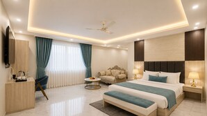Ein modernes Hotelzimmer mit einem großen Bett, einem Schreibtisch, einem Sessel, einem runden Couchtisch, einer Couch und einem Fernseher.