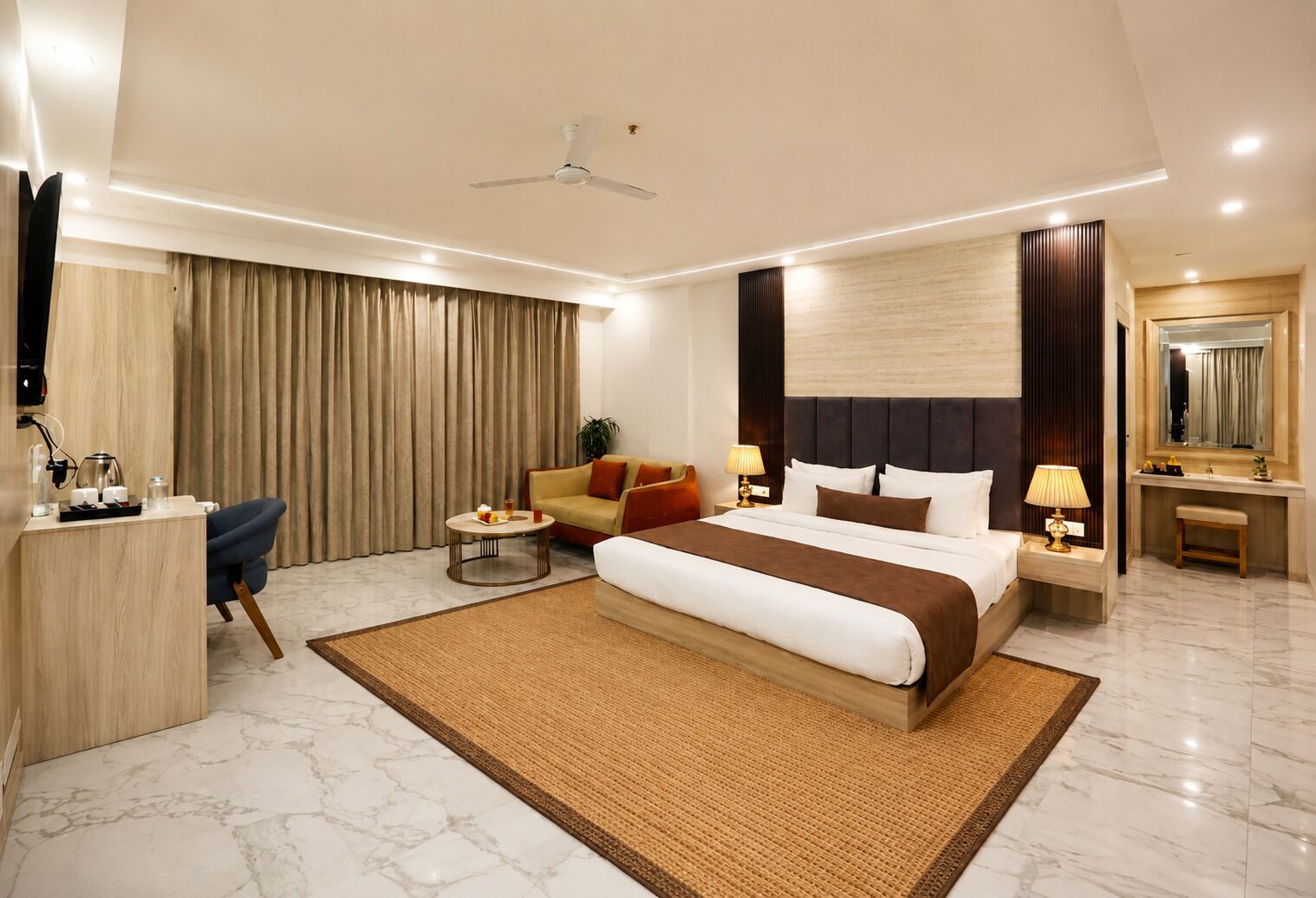Una habitación de hotel moderna con una cama grande, un escritorio con silla, un sofá, una mesita de noche con lámpara y un baño con espejo y lavamanos.