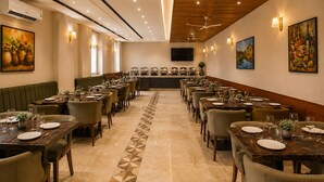A hotel dining area with multiple tables, chairs, and a central buffet. - Hotel West End Mahipalpur Delhi IGI (New Delhi)