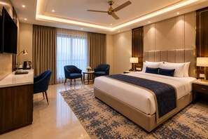 Habitación de hotel con una cama grande, un escritorio, dos sillas, una mesita y un ventilador de techo.