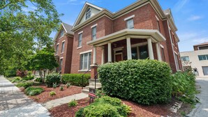 A two-story brick house with a front porch, a well-maintained garden, and a 'For Sale' sign.