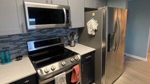 A modern kitchen with grey cabinets, a stainless steel refrigerator, a microwave, an oven, and a stove.