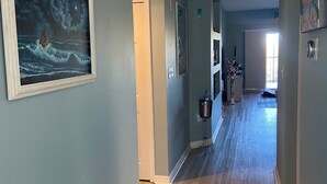 A hallway with light blue walls, wooden flooring, and a framed painting of a ship on the left.