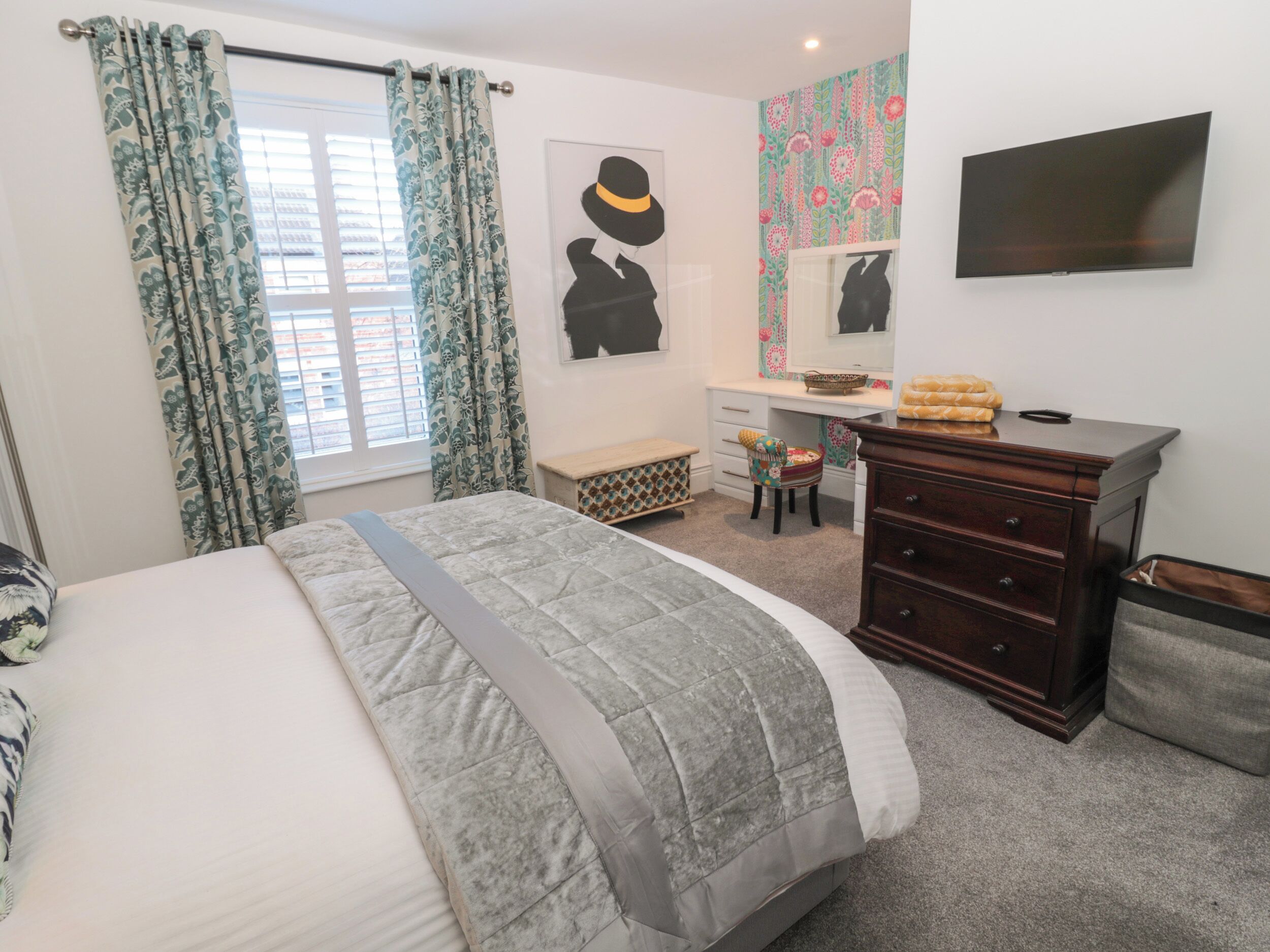A bedroom with a bed, a dresser, a desk, a chair, and a television.