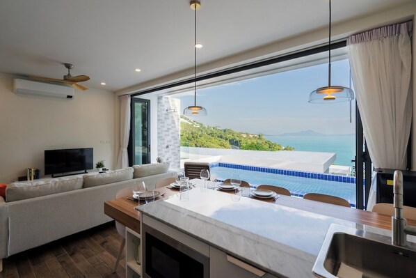 A modern kitchen with a dining area, a television, and a view of a pool and landscape.