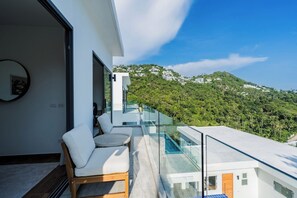A modern balcony with a glass railing overlooking a lush green hillside.