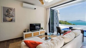 A modern living room with a large window, a flat-screen TV, a sofa, and a view of the sea.