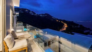 A modern balcony with a glass railing overlooking a coastal view at dusk.