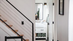 Eine Treppe führt zu einem Badezimmer mit einem weißen Waschbecken, einem Spiegel und einem Handtuchhalter.