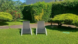 Twee terrasstoelen in een verzorgde tuin met strakke hagen en diverse planten.