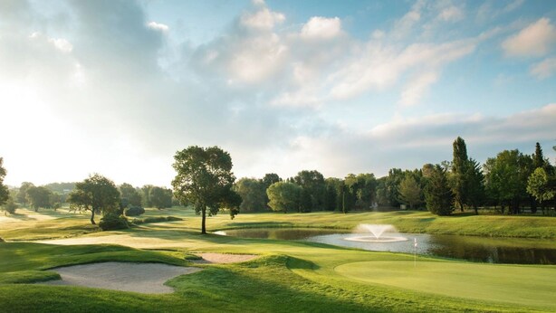 Een golfbaan met een vijver, bomen en een vlag op een green.