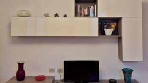 A modern living room with a flat-screen TV, a white entertainment unit, a chandelier, and a bookshelf.