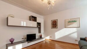 A modern living room with a flat-screen TV, built-in shelves, and a chandelier.