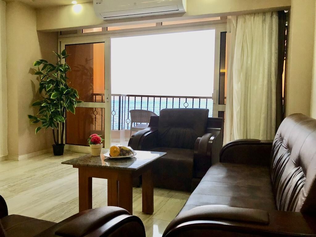 A living room with a sofa, a table with a plant, and a view of the outside.