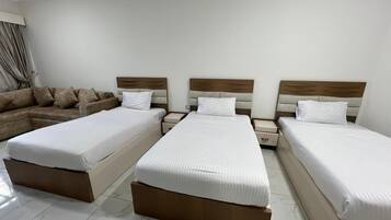 A hotel room with three single beds, a sofa, and a nightstand.