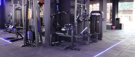 A gym with various exercise machines, a mirrored wall, and a tiled floor.