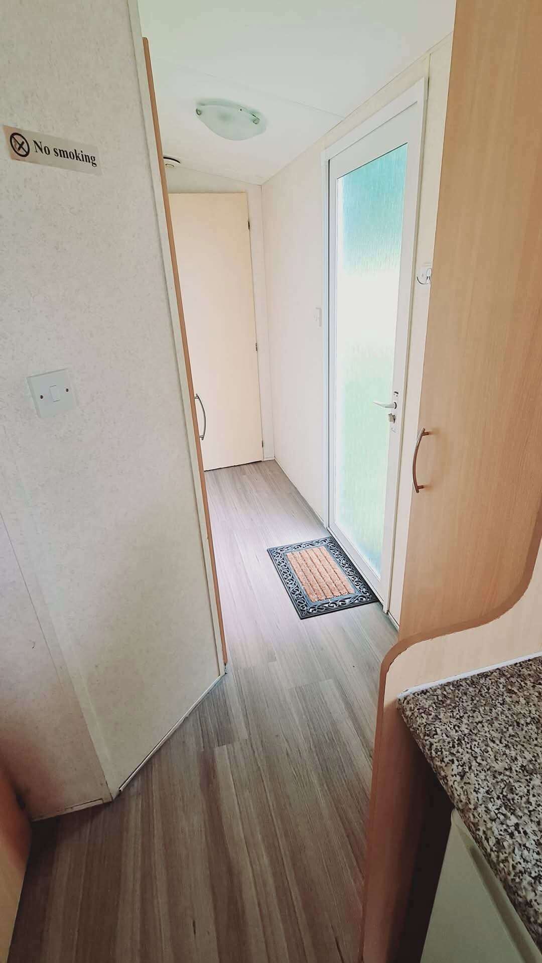 A narrow hallway with a 'No smoking' sign, a door leading to a balcony, and a doormat.