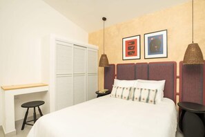 Een slaapkamer met een bed, een bureau, twee stoelen, een kledingkast en twee aan de muur hangende foto's.