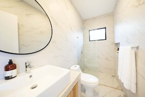 A bathroom with a marble wall, a sink with a soap dispenser, a toilet, and a shower area.
