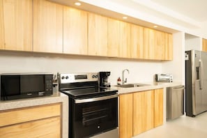 A modern kitchen with wooden cabinets, a microwave, stove, sink, and a refrigerator.