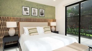 A modern bedroom with a bed, two bedside tables, a wall-mounted air conditioner, and a large window with a view of greenery. - Casa Usure – Huetar-Inspired Beachside Haven (Provincia de Puntarenas)