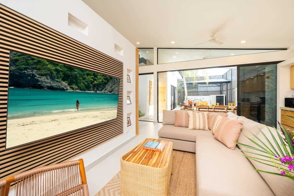 A modern living room with a large TV, a sofa, a coffee table, and a view of a beach.