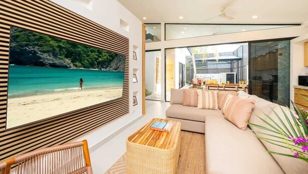 A modern living room with a large TV, a sofa, a coffee table, and a view of a beach. - Casa Usure – Huetar-Inspired Beachside Haven (Provincia de Puntarenas)