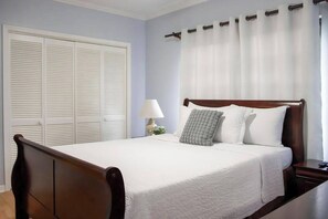 A neatly made bed with white linens, a wooden headboard, and a nightstand with a lamp.
