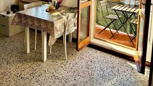 A room with a dining table, chairs, a window with a view of a tiled roof, and an open door leading to an outdoor area with a table and chairs. - At the Biennale at Leda's (Venezia)