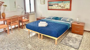A bedroom with a bed, a desk, a chair, a radiator, a window, and a painting on the wall. - At the Biennale at Leda's (Venezia)